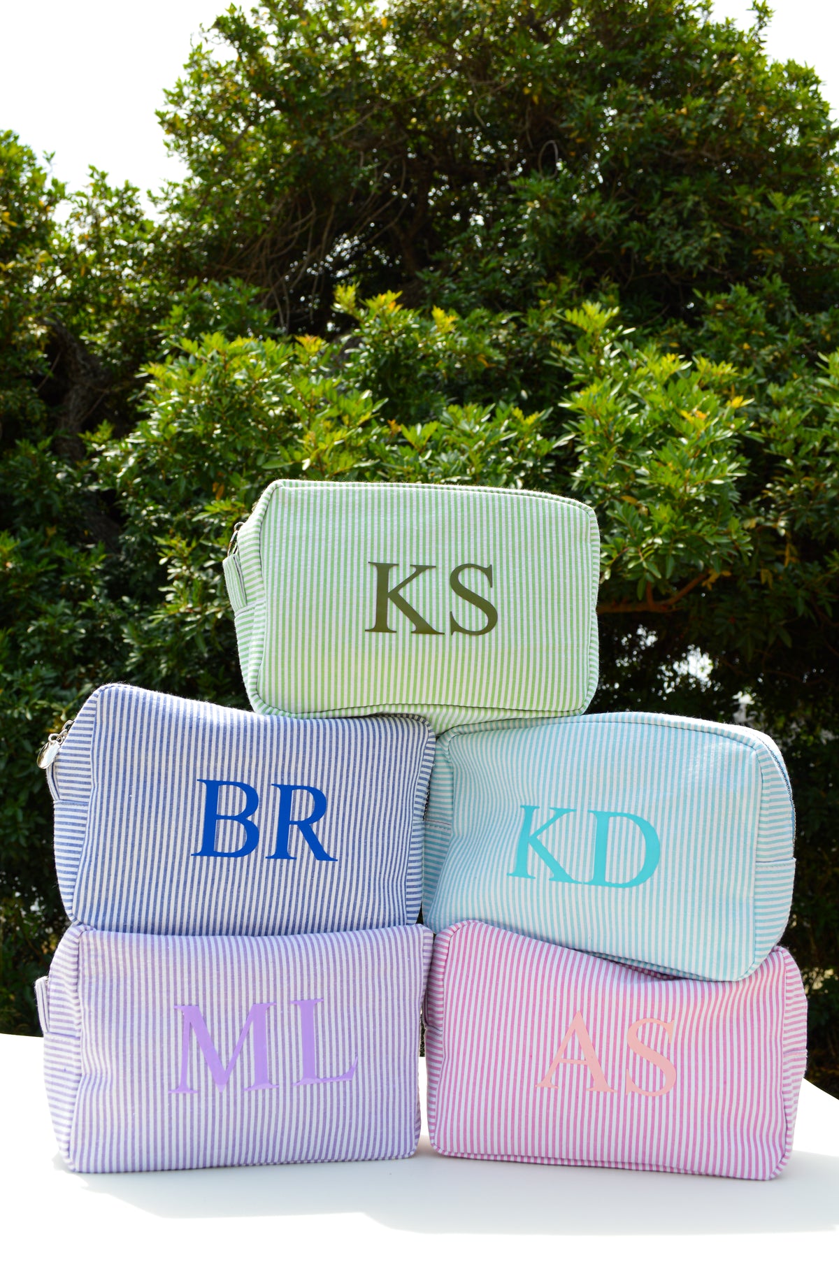 Group of striped bags with monogram initials in front of a leafy background