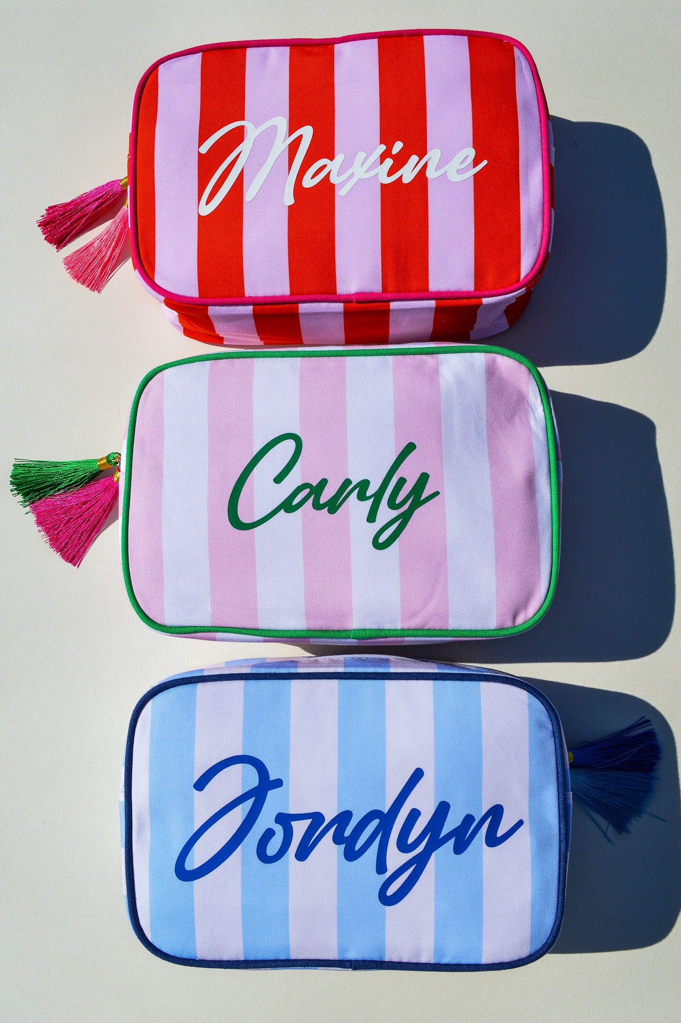 Three striped pouches with names 'Maxine', 'Carly', and 'Jordyn' on a light background.