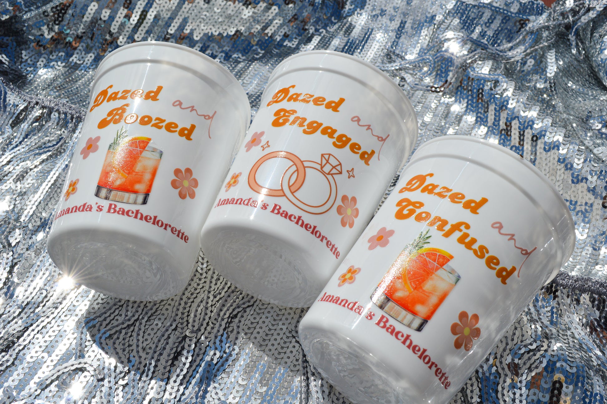 Three cups with humorous bachelorette party-themed text on a reflective surface.
