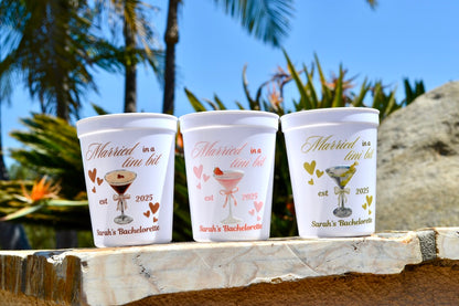 Three personalized cups with text and graphics on a wooden surface with a tropical background.