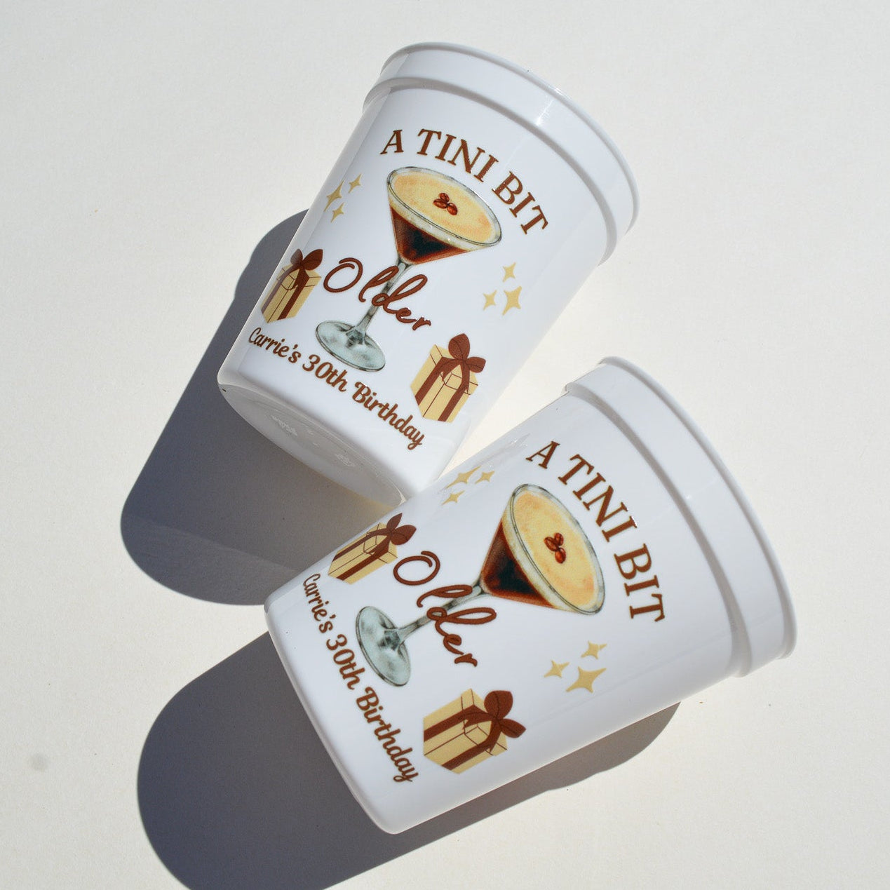 Two 'A Tini Bit' white plastic cups on a white surface