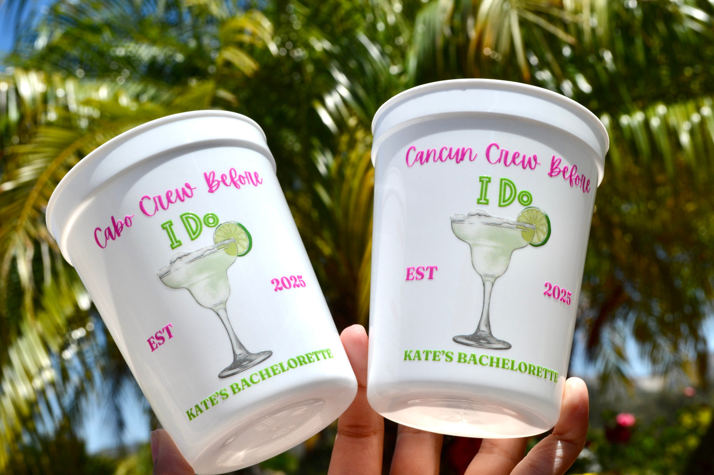 Two plastic cups with personalized designs and text, held against a blurred green outdoor background.