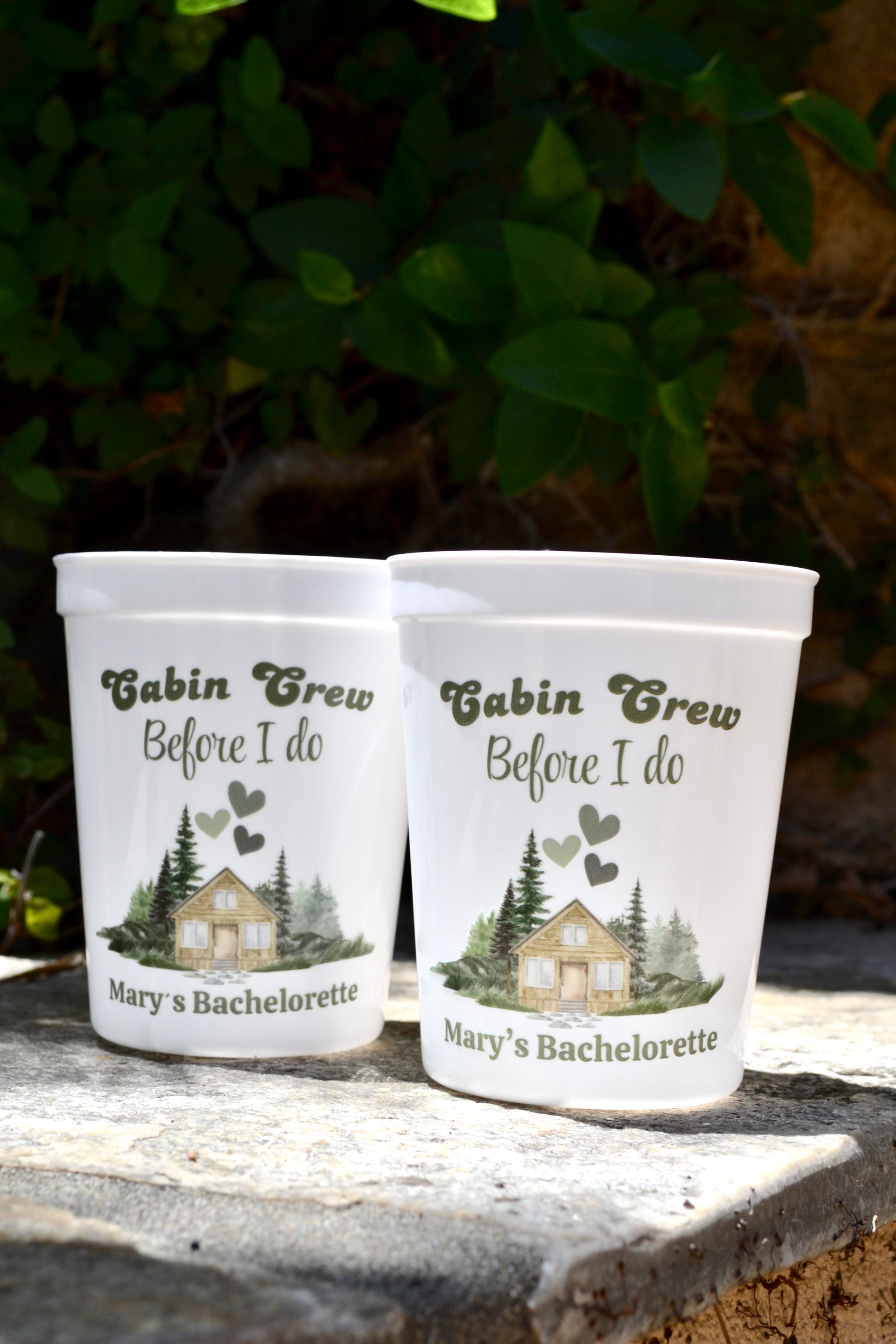 Two personalized cups with 'Cabin Crew Before I Do' design on a stone surface with greenery in the background.